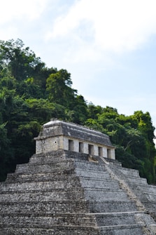 An ancient stone pyramid structure surrounded by dense green jungle vegetation, showcasing a blend of man-made architecture and natural beauty under a bright blue sky.