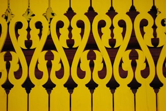 Intricate, symmetrical patterns form a decorative design with a repeating motif. The design is cut out of yellow material, creating a contrasting effect against a darker background.