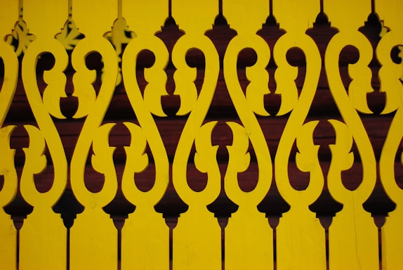 Intricate, symmetrical patterns form a decorative design with a repeating motif. The design is cut out of yellow material, creating a contrasting effect against a darker background.