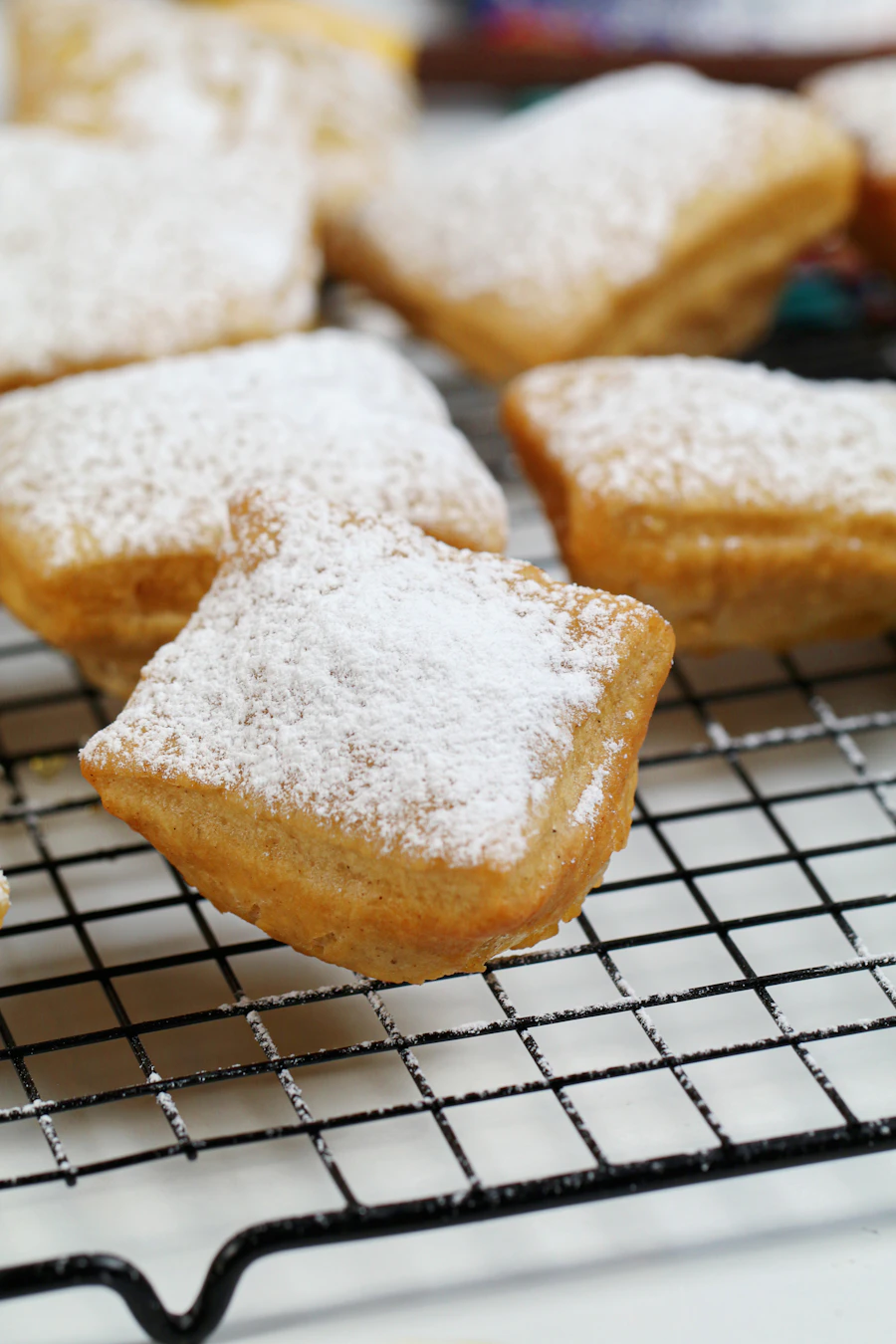 Square beignets dusted with powdered sugar cooling on a black wire rack
