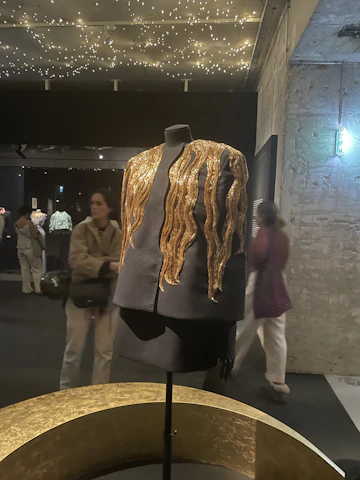 A sleek black mannequin dressed in a deep burgundy, gold-accented prom gown under soft moody lighting.