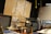 A workshop or maker space containing tools and equipment is shown. Pegboards with various hand tools like screwdrivers, wrenches, and tape are mounted on the wall. Large tool chests and cabinets are placed beneath the pegboards. The room has a high ceiling with industrial black piping and hanging yellow cords. A logo with a wrench and screwdriver symbol is prominently displayed on a large wooden board.