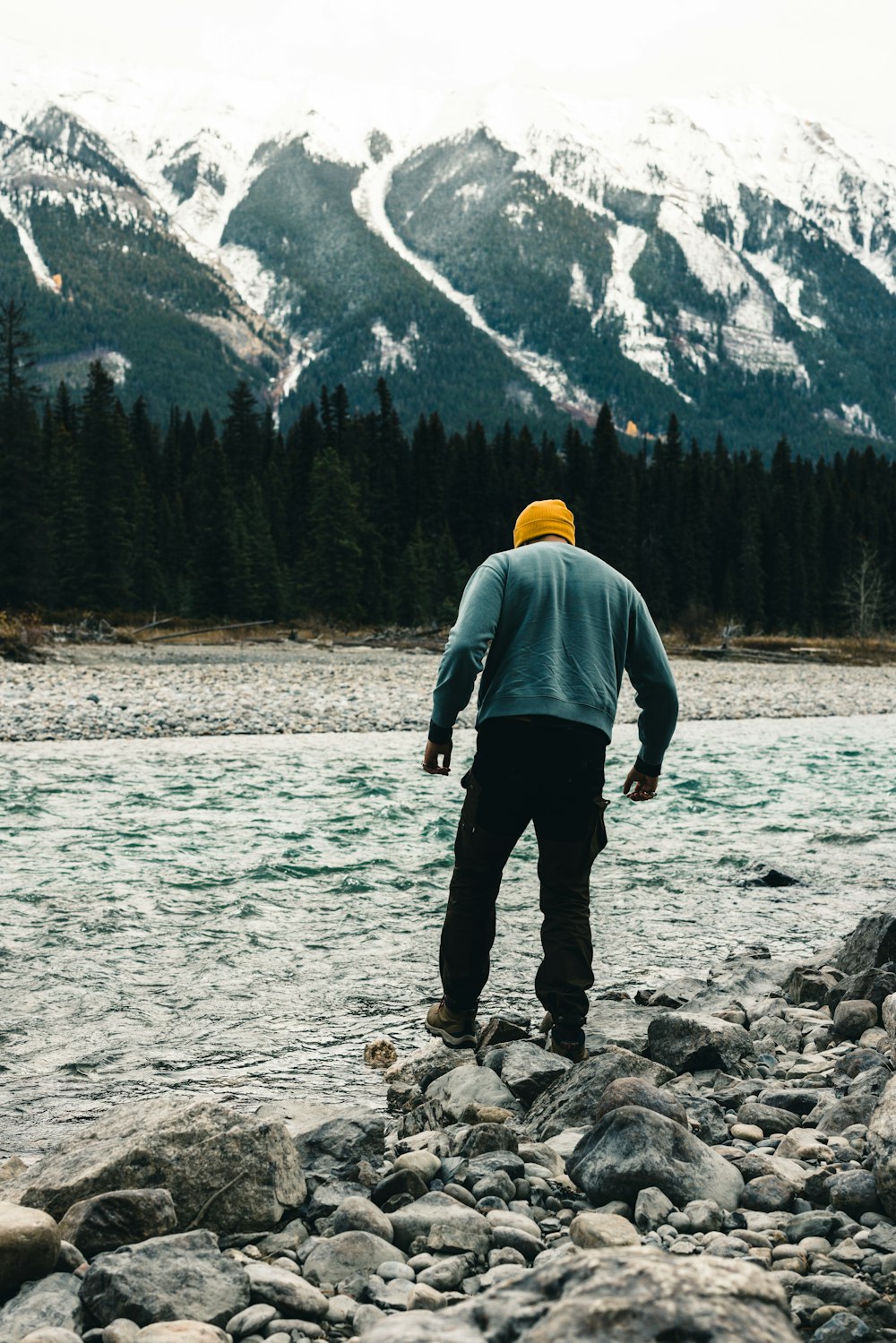 Un uomo che cammina su un letto roccioso del fiume con una montagna sullo sfondo