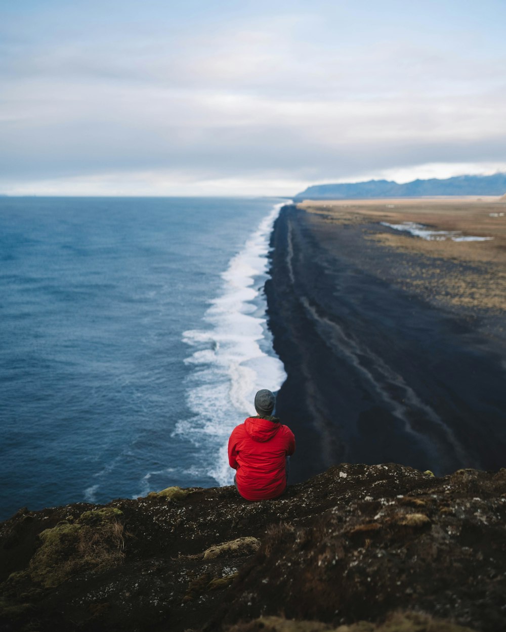 a person sitting on a rock looking at the ocean