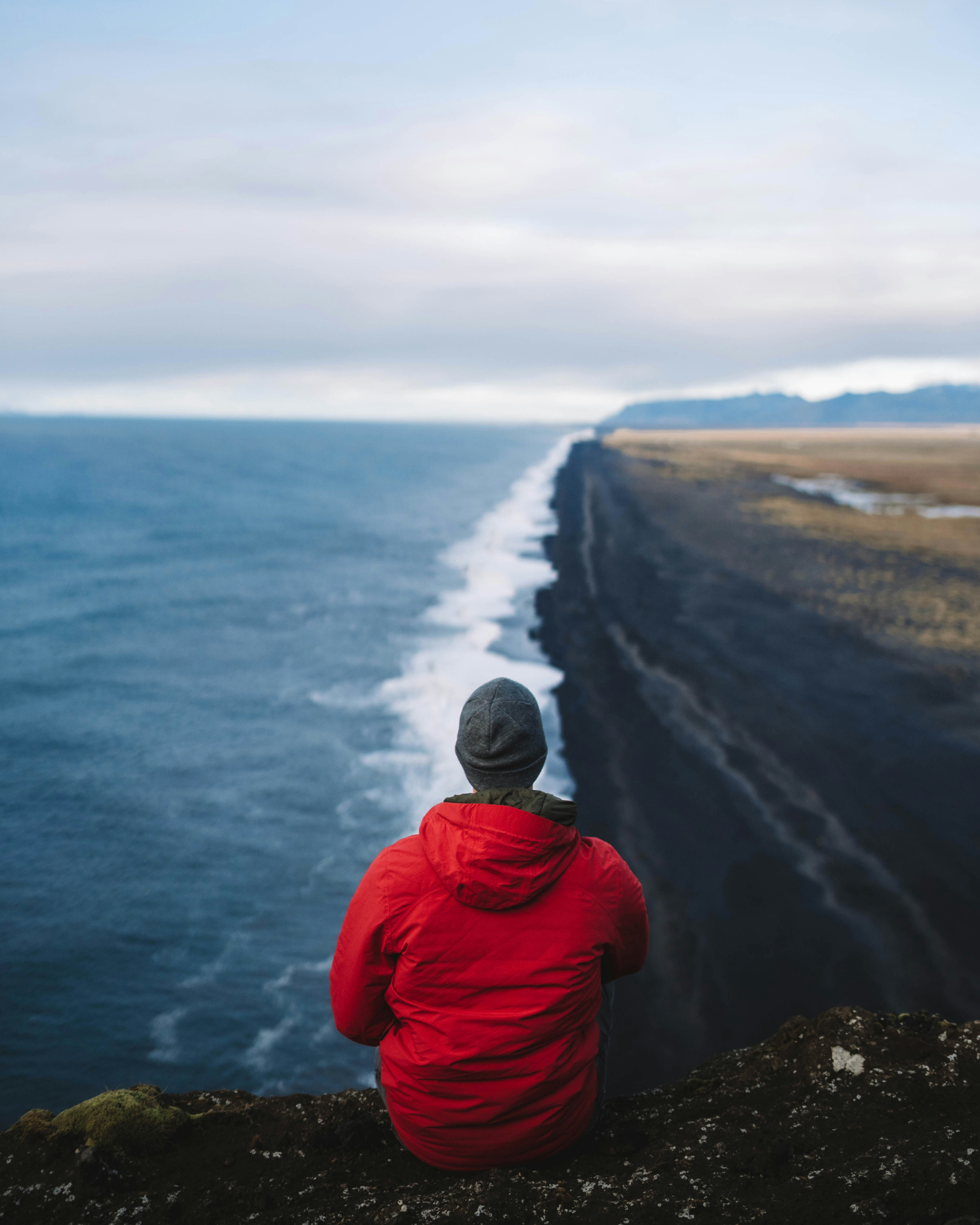 A person sitting on a rock looking out at the ocean photo – Free Vik ...