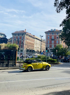 A bright yellow city car cruising past a famous Paris landmark under a clear sky.