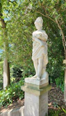 An antique iron ornamental statue standing gracefully beside a blooming garden path.