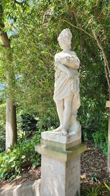 An antique iron ornamental statue standing gracefully beside a blooming garden path.