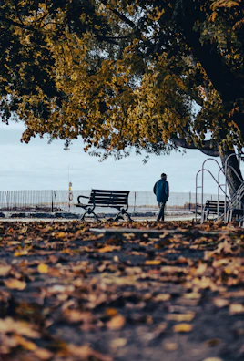 A thoughtful individual walking alone in a quiet park, surrounded by autumn leaves.