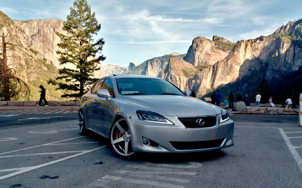 a silver car parked in a parking lot with people and mountains in the background