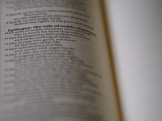 A close-up view of an open book with text discussing the qualities of a wife of noble character. The focus is on a specific passage, while the rest of the text is blurred, creating a depth of field effect.