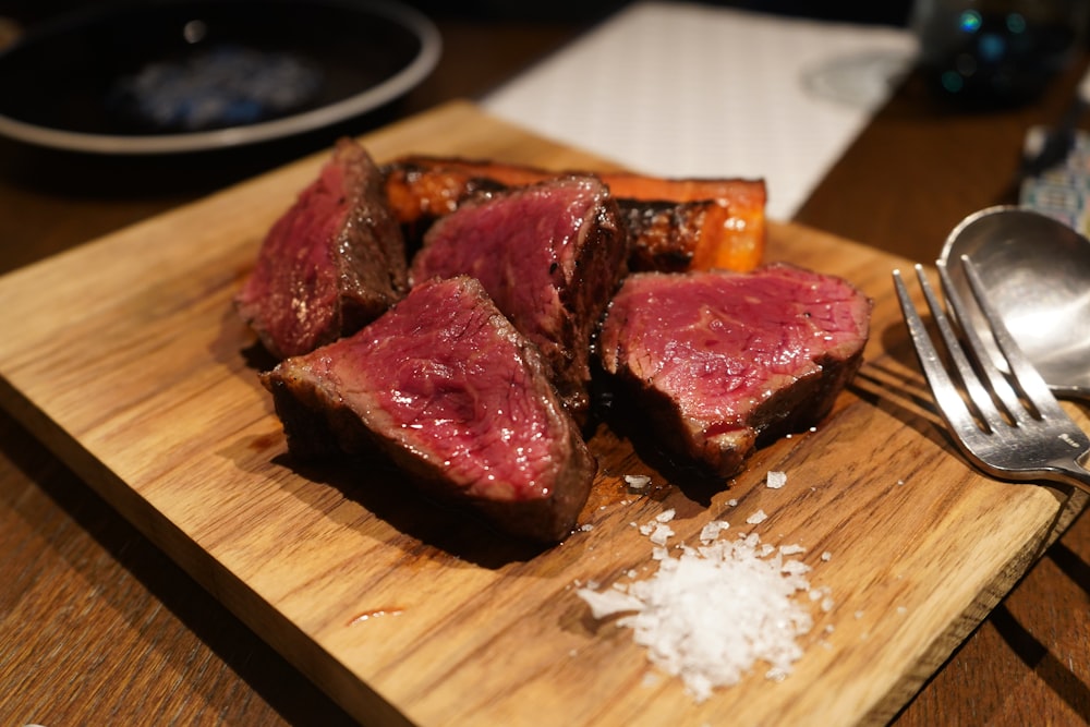 a piece of meat on a cutting board with a fork and spoon