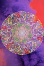 A vibrant mandala with intricate patterns, featuring a combination of floral and geometric designs. The mandala is filled with vivid colors, primarily purples, greens, and reds, and is set against a background of swirling purple and orange clouds, creating a mystical and dreamlike atmosphere.