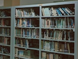 Bookshelves filled with a variety of books organized neatly in a library setting, with labels indicating different sections.