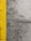 A close-up view of a concrete surface with a bright yellow painted line running vertically along the left side. The concrete appears textured with small holes and patches of discoloration, showcasing signs of wear and use.