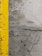 A close-up view of a concrete surface with a bright yellow painted line running vertically along the left side. The concrete appears textured with small holes and patches of discoloration, showcasing signs of wear and use.