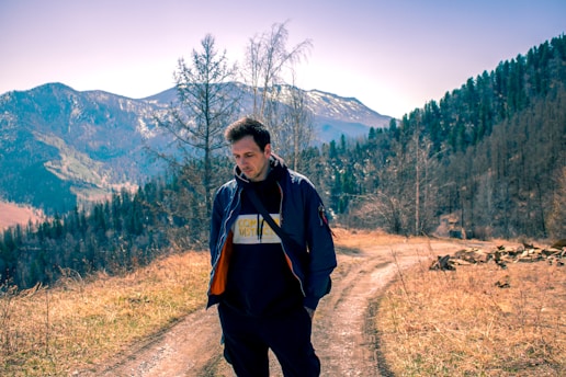 a man standing on a dirt road in front of a mountain