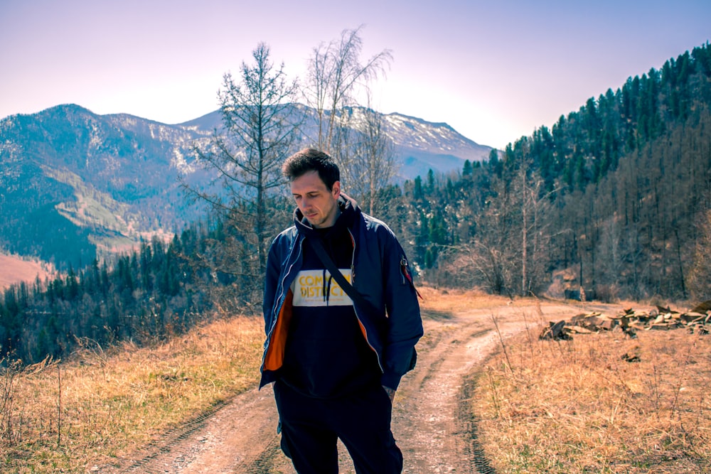 a man standing on a dirt road in front of a mountain