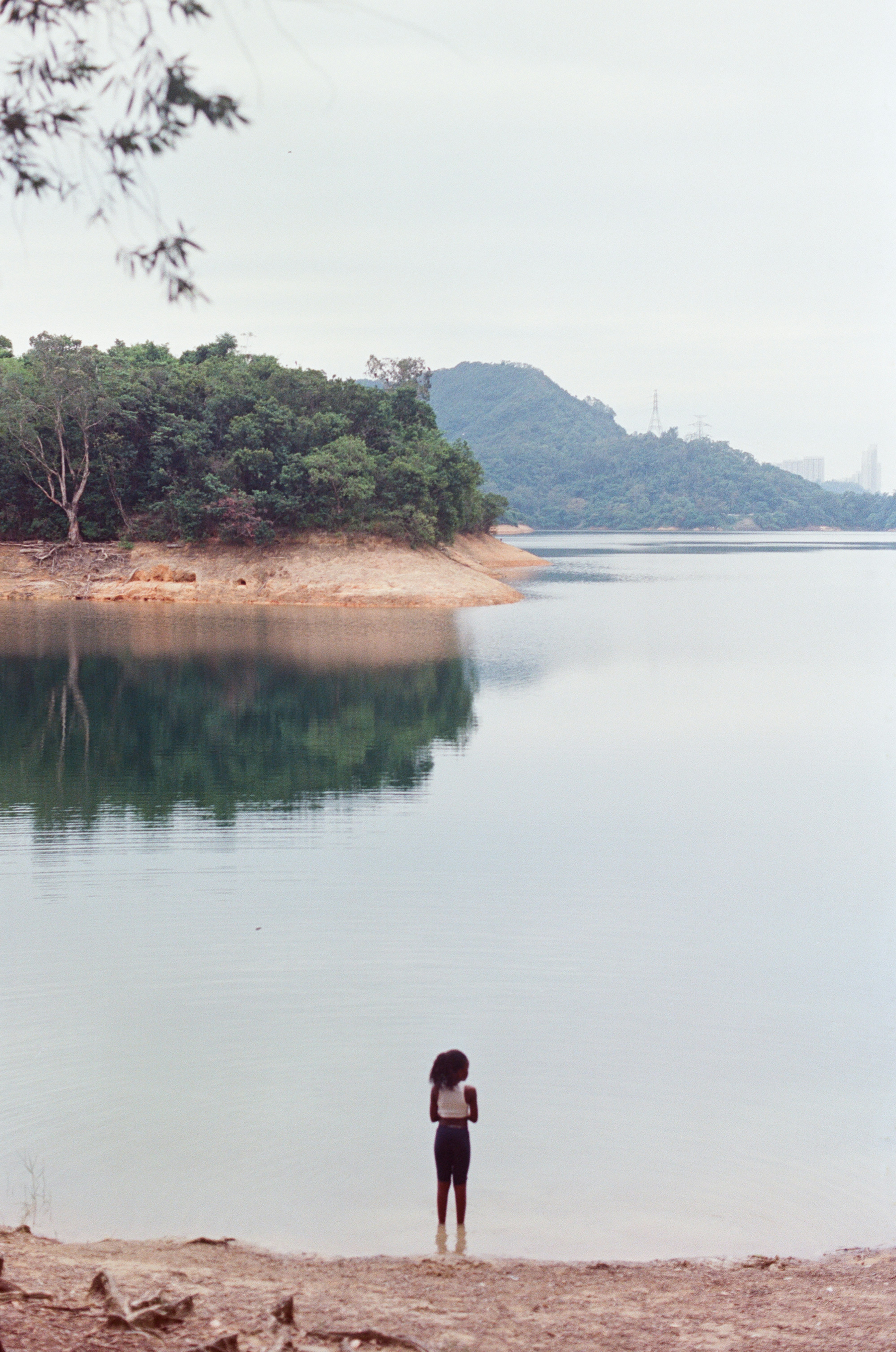 a man standing in a body of water with trees and hills in the background