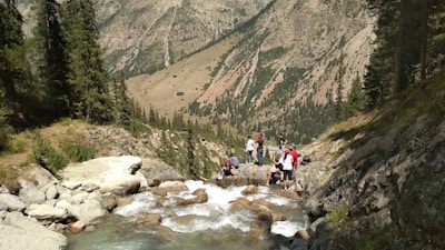 A group smiling and resting beside a clear mountain stream during a guided tour.
