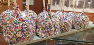 Close-up of a handcrafted candy apple with cinnamon, wrapped in clear cellophane on a rustic wooden table.