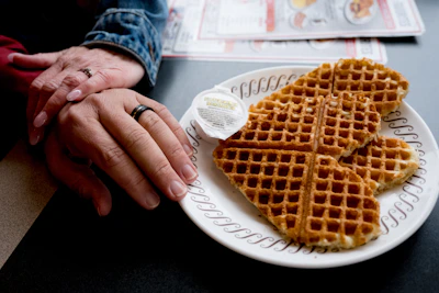 Bright and cheerful display of heart-shaped waffles topped with strawberries and syrup on a rustic wooden table.
