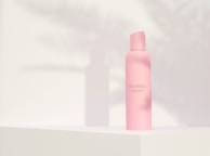 Close-up of a pastel pink skincare bottle with a simple label on a clean, light surface.