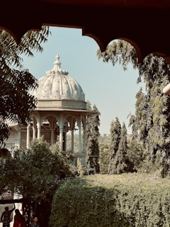 A charming pavilion nestled in a sunlit green park with blooming trees, inviting visitors to connect.