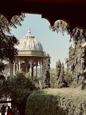 A charming pavilion nestled in a sunlit green park with blooming trees, inviting visitors to connect.
