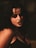 A person with dark hair and intense makeup, featuring dark eyeshadow and lipstick. Red, vein-like details are painted around the eyes, creating a dramatic and eerie appearance. The setting has low lighting, adding a mysterious and gothic vibe.