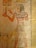 A wall painting showing an ancient Egyptian figure in profile, wearing traditional attire with a headdress. They hold a small object adorned with an ankh and a statue. Hieroglyphics are present above the figure, and additional artwork is visible at the bottom of the frame.