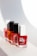 Four nail polish bottles are arranged in a line, each featuring different colors and brands. The bottles have square caps, with the closest one being red and white, followed by an orange, a pink, and another red bottle in the background. The light casts soft shadows behind them, creating a clean and minimalistic setting.