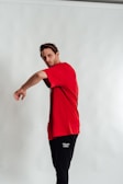 A person wearing a bright red t-shirt and black pants with 'Team USA' written on them poses against a plain, light-colored background. The pose appears dynamic, with the left arm extending outward.