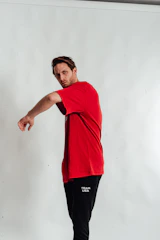 A comfortable black New Stance t-shirt with a bold red and gold graphic, worn by a smiling fan at a flag football game.