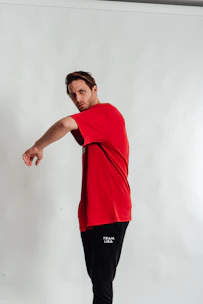 A comfortable black New Stance t-shirt with a bold red and gold graphic, worn by a smiling fan at a flag football game.