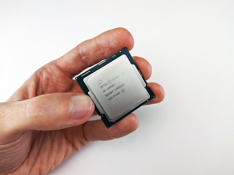 A close-up view of a person holding a computer processor, featuring an Intel Core i9 label. The processor is held between the thumb and index finger, with a plain white background creating a clean and minimalistic setting.