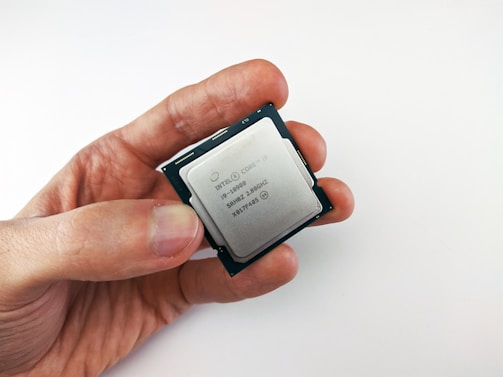 A close-up view of a person holding a computer processor, featuring an Intel Core i9 label. The processor is held between the thumb and index finger, with a plain white background creating a clean and minimalistic setting.