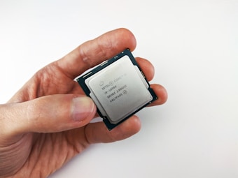 A close-up view of a person holding a computer processor, featuring an Intel Core i9 label. The processor is held between the thumb and index finger, with a plain white background creating a clean and minimalistic setting.