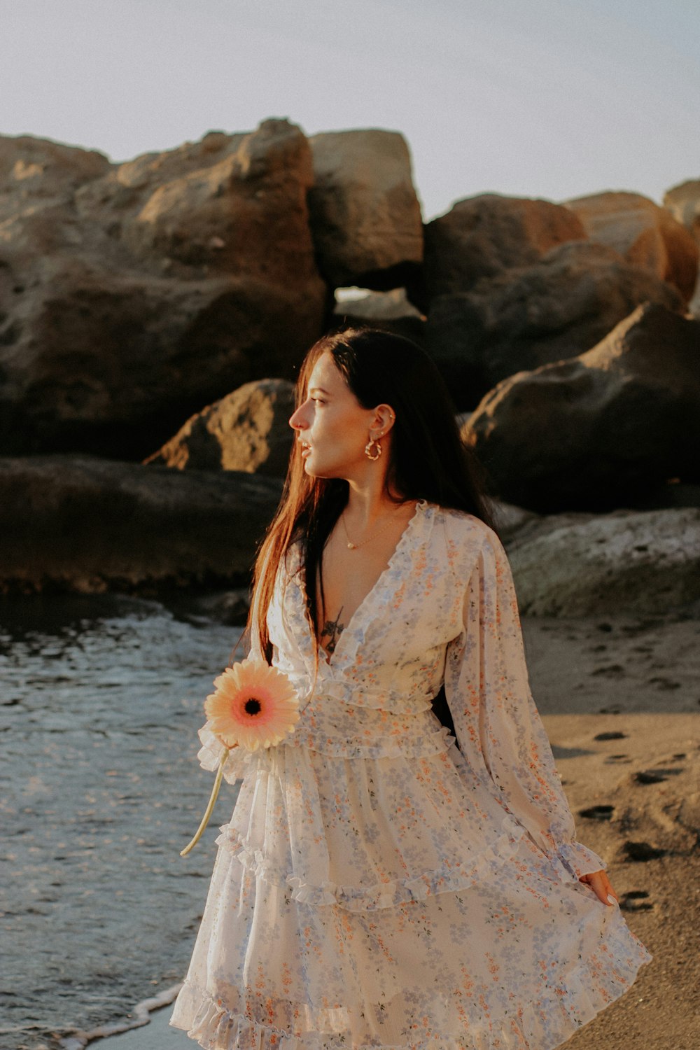 a person in a white dress on a beach with a flower in the hand