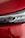 A close-up of a car's headlight against a glossy red surface, showing the intricate design of the headlight along with reflections on the surrounding bodywork.