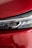 A close-up of a car's headlight against a glossy red surface, showing the intricate design of the headlight along with reflections on the surrounding bodywork.