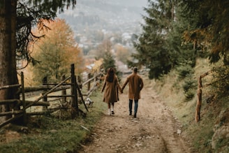 a man and woman walking on a dirt path in the woods