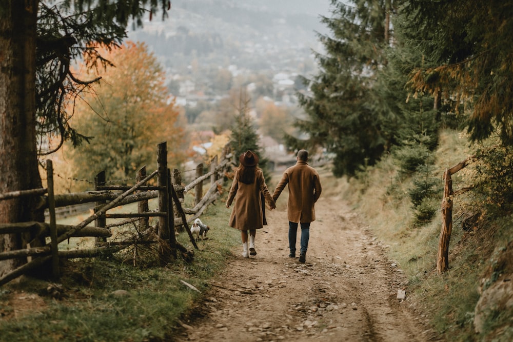 a man and woman walking on a dirt path in the woods