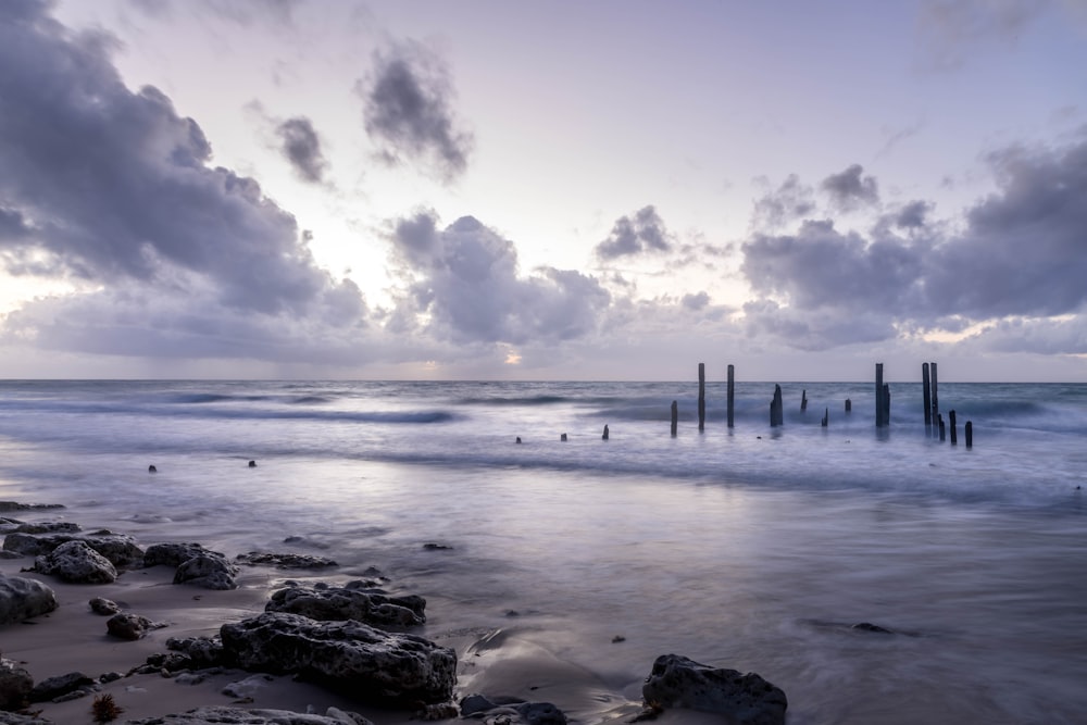 a beach with rocks and a body of water with a cloudy sky