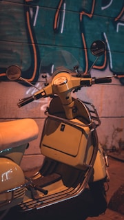 A neon-lit scooter parked against a graffiti-covered wall at night, glowing with vibrant green and electric blue hues.