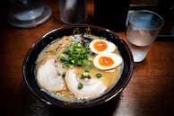 A minimalist bowl of shoyu ramen with tender pork slices and crisp bamboo shoots on a simple wooden table.