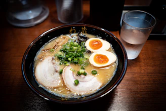 A minimalist bowl of shoyu ramen with tender pork slices and crisp bamboo shoots on a simple wooden table.