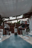 A rustic wooden table set outdoors with glasses of red wine and vineyard views in the background.
