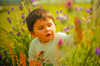 A candid shot of a toddler exploring nature, reaching out to touch a bright flower.