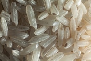Close-up view of numerous grains of white rice with a variety of sizes and slight translucence, highlighting the texture and structure of each grain.